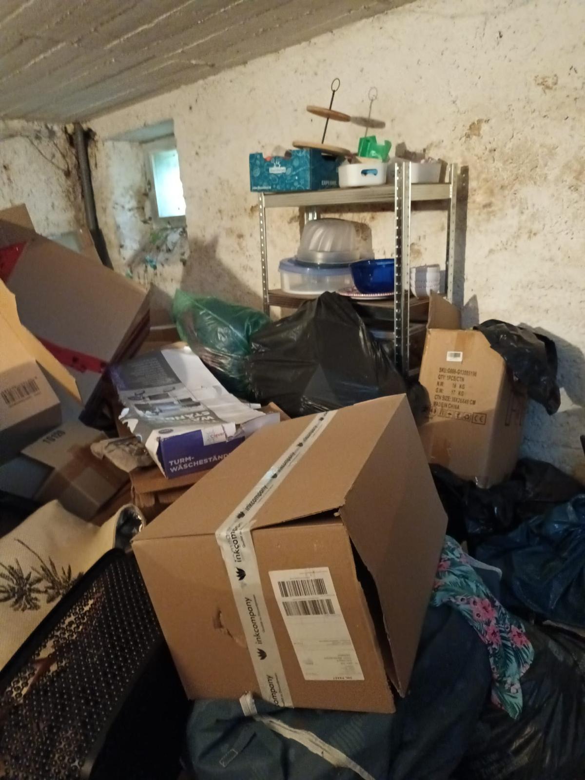 Gefüllter Keller vor einer Entrümpelung mit Kartons, Säcken und Regalen